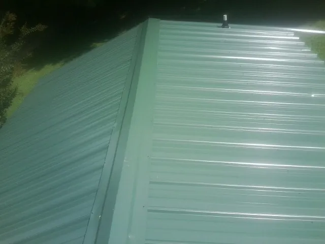 New green metal panels meeting at the ridge of a roof — Flat Roof Repair work by our crew in Stanley
