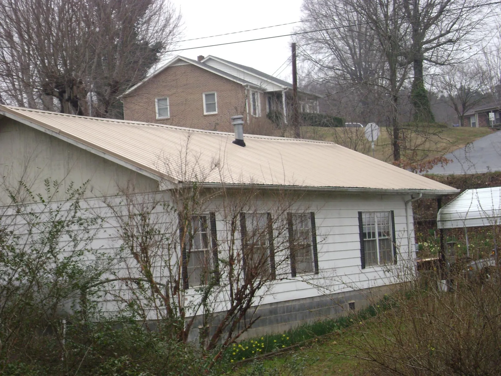 Tan metal roof on a white sided house set into a hillside — Commercial Roofing by Roofing Brothers in Stanley